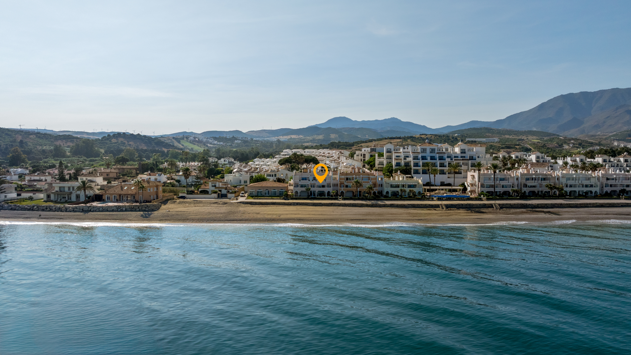 Drone view of Playa del Moral beachfront apartment complex with sea and mountain backdrop in Costa del Sol.