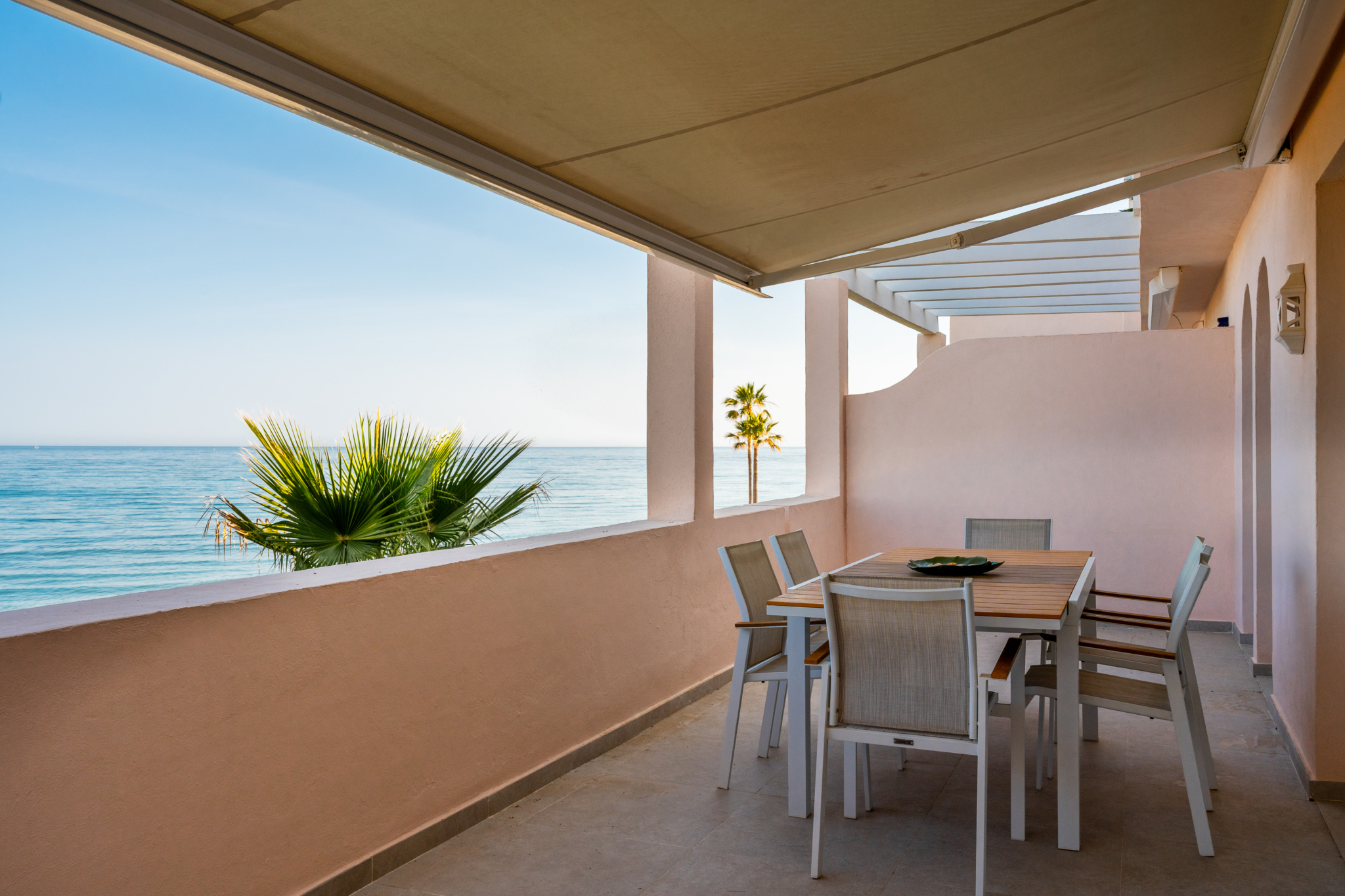 Seafront terrace with outdoor dining area, awning, and Mediterranean views at Playa del Moral apartment.