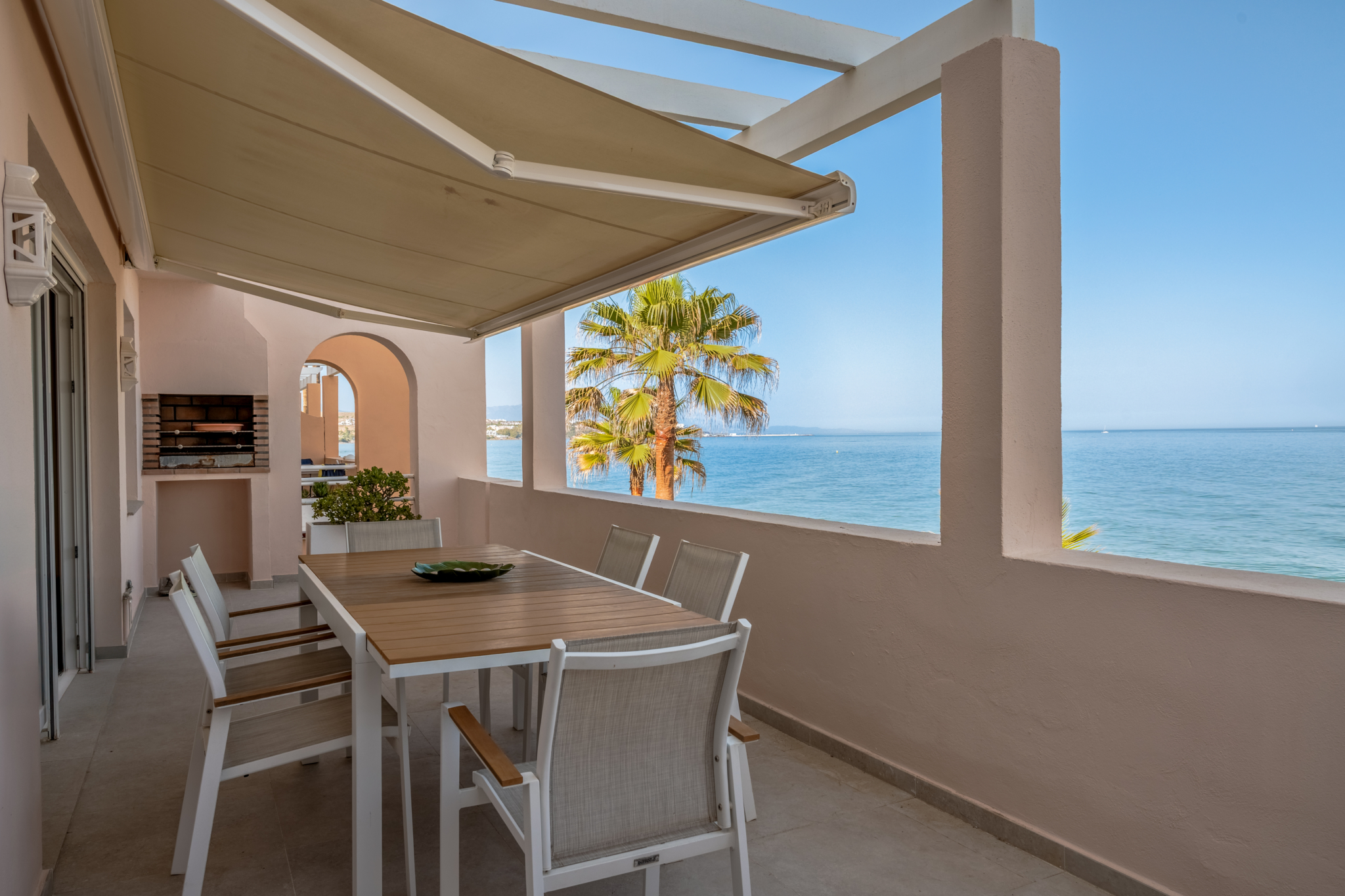 Seafront terrace with outdoor dining area, awning, and Mediterranean views at Playa del Moral apartment.
