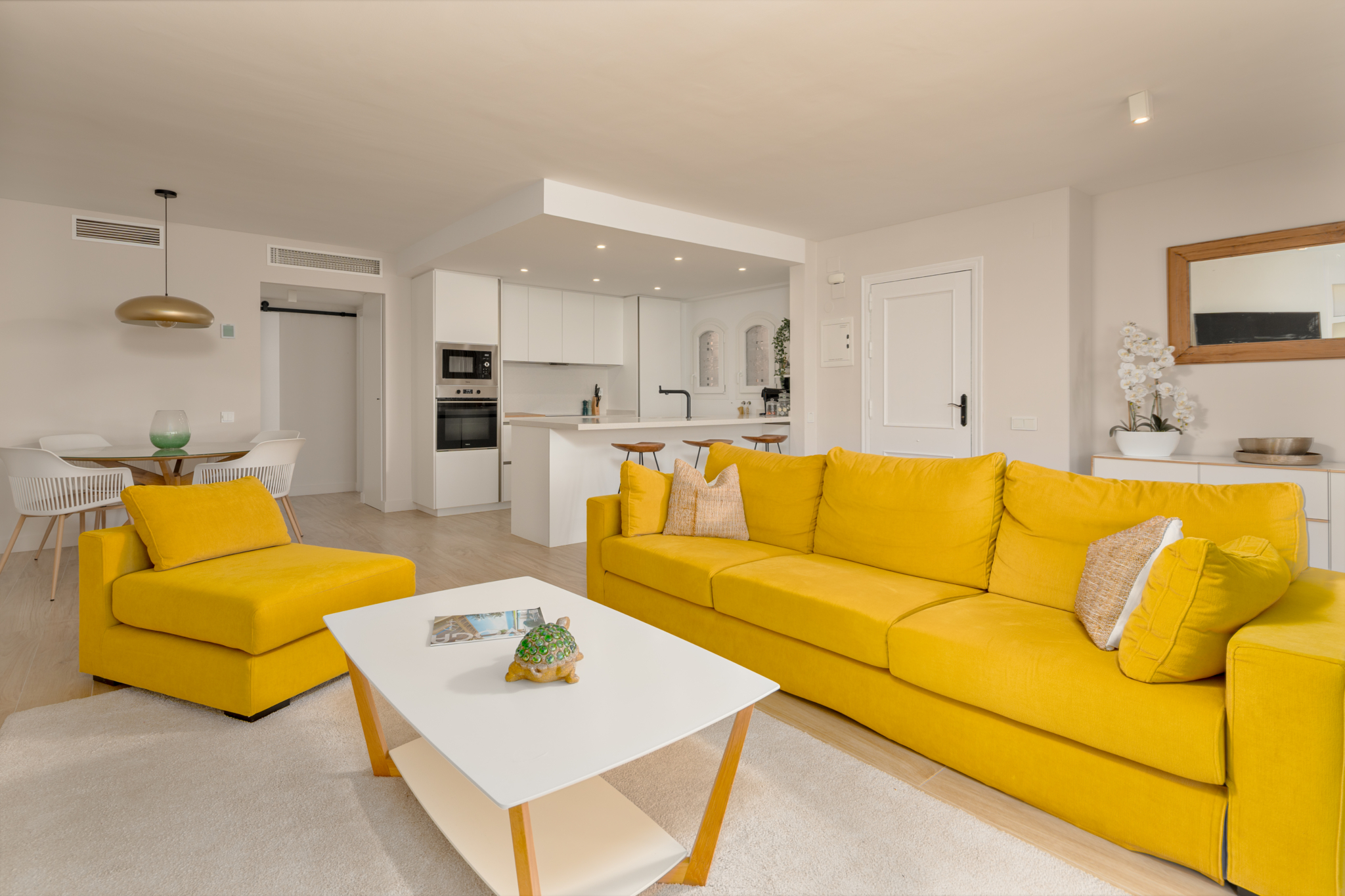 Bright open-plan living room with yellow sofa, modern kitchen, and dining area in Playa del Moral apartment