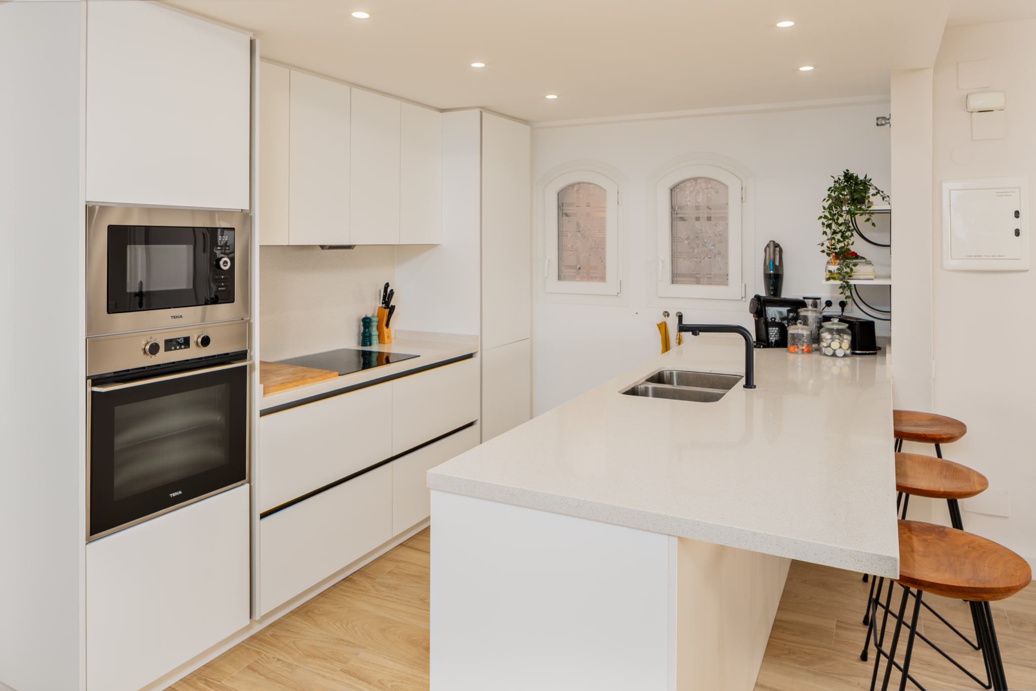 Contemporary white kitchen with breakfast bar, built-in appliances, and natural light in Playa del Moral apartment.
