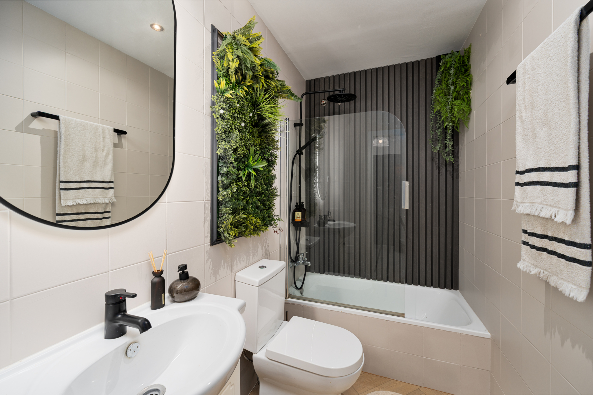 Modern bathroom in Bel-Air semi-detached house near Marbella with sleek black shower fittings, vertical wood panels, and green wall feature.