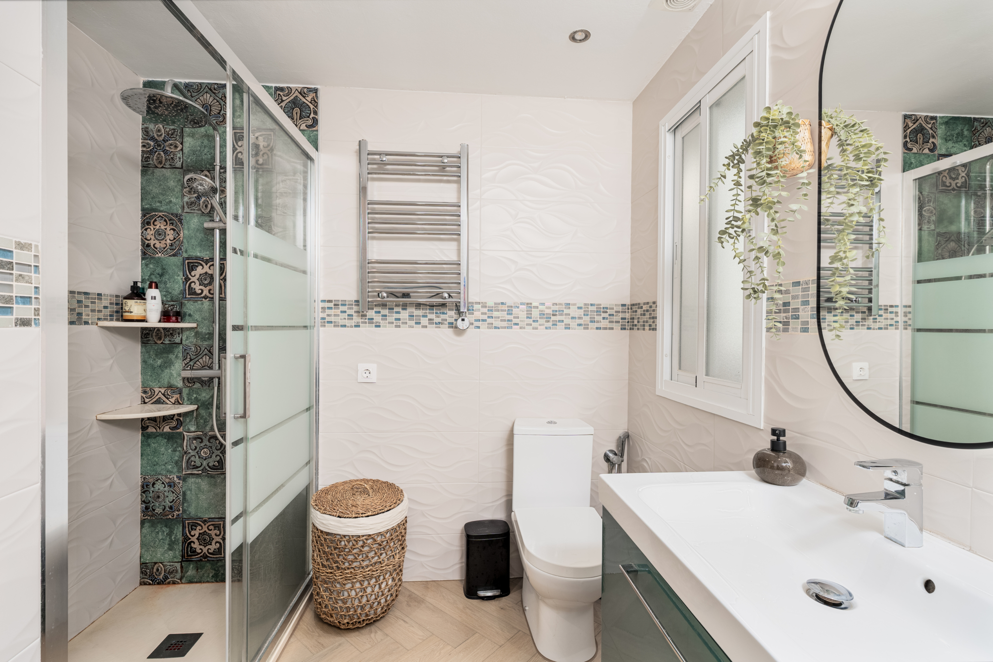 Modern bathroom interior in Bel-Air semi-detached house near Marbella, featuring glass shower, white tiles, green vanity, and decorative mosaic details.