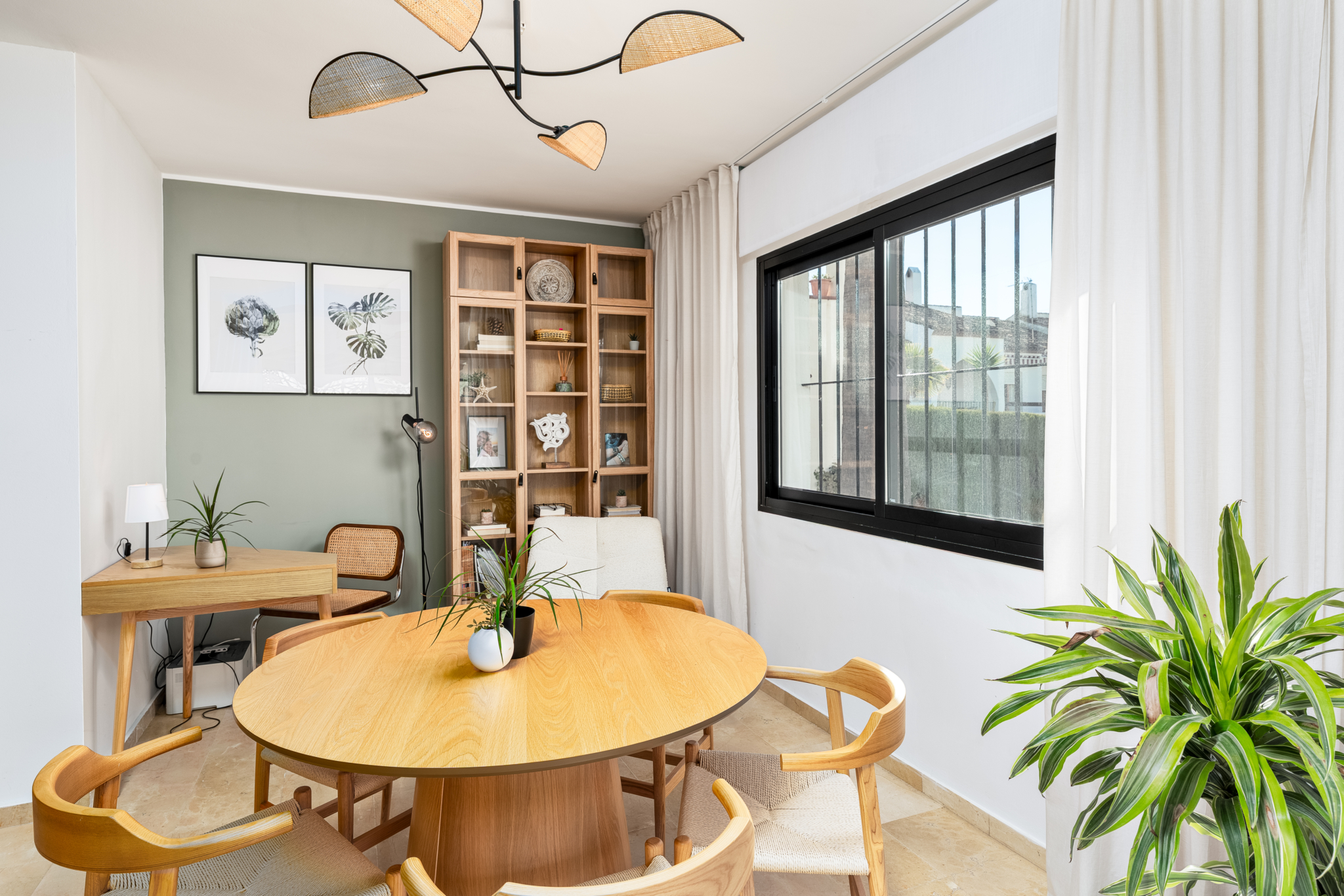 Bright modern dining room with wooden round table, mid-century chairs, indoor plants, and large window in Bel-Air semi-detached house.