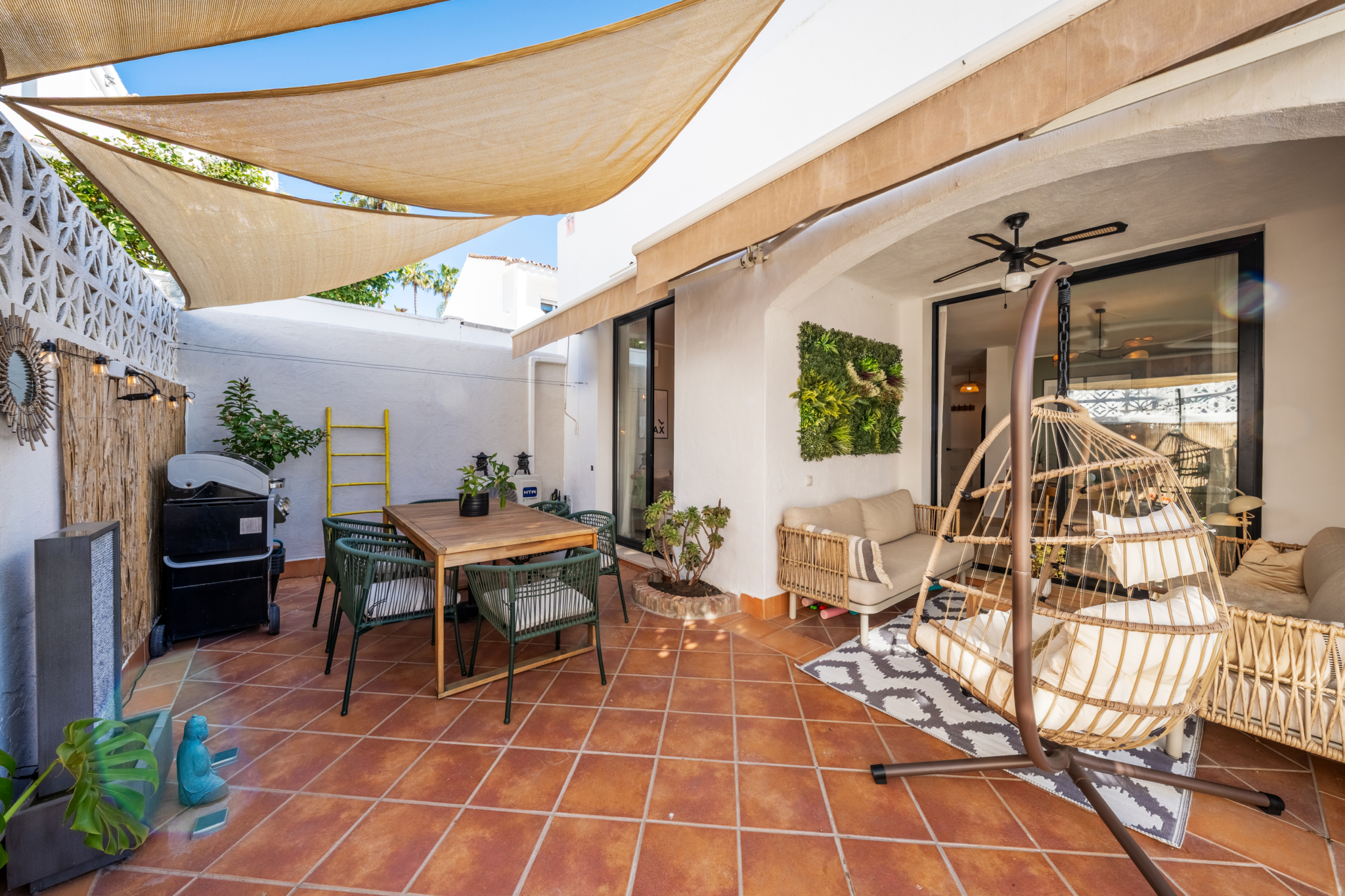 Stylish covered terrace at Bel-Air semi-detached home near Marbella, featuring terracotta tiles, outdoor dining area, hanging chair, and Mediterranean decor.