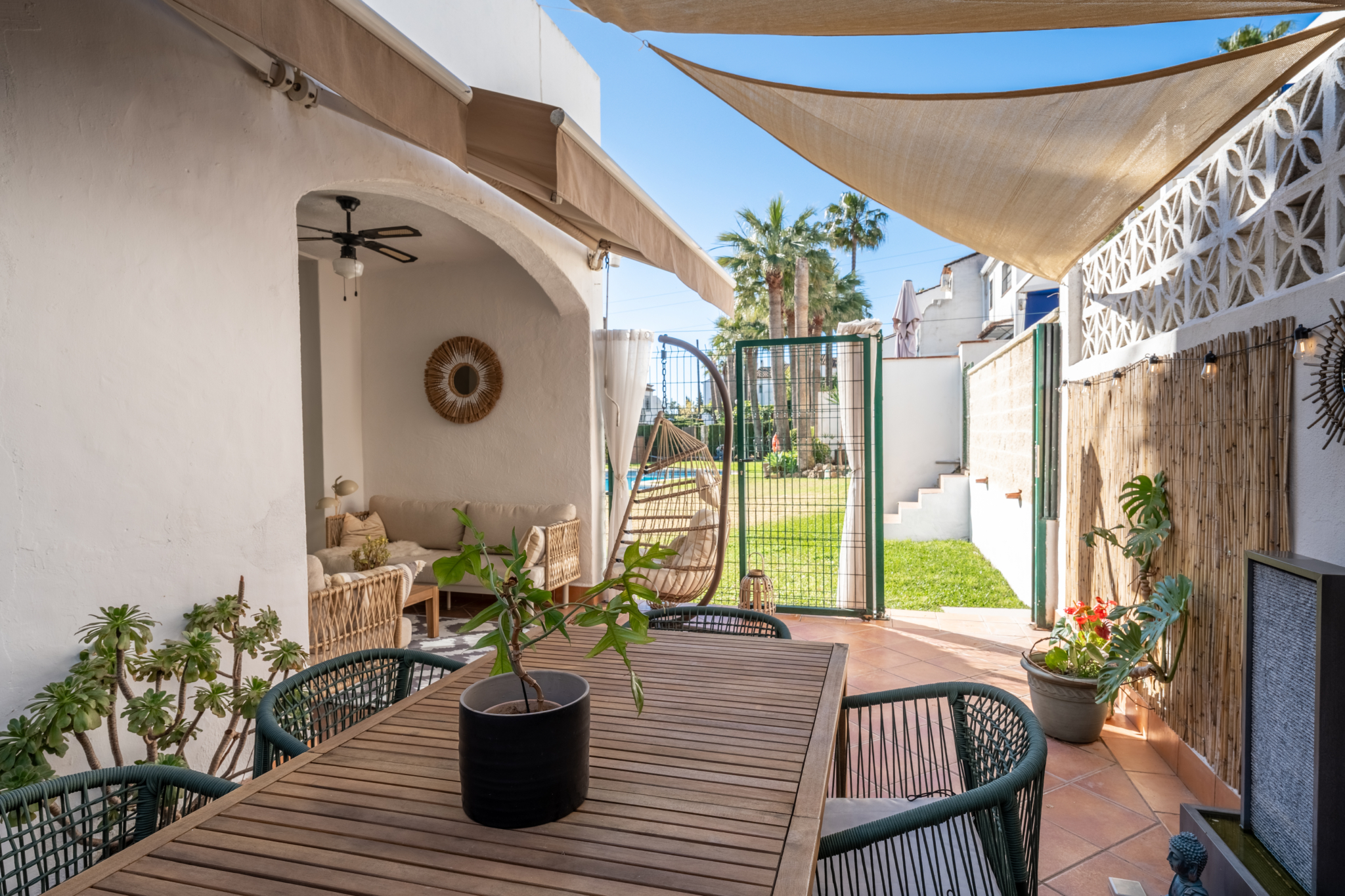 Outdoor patio and garden area of Bel-Air semi-detached house near Marbella, featuring dining table, sun shades, rattan furniture, and pool access