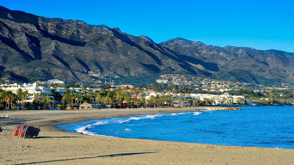 Beautiful beach and coastal skyline in Nueva Andalucía with mountains in the background, showcasing the area for new property developments in Marbella and highlighting the average rental yields for properties in Estepona.