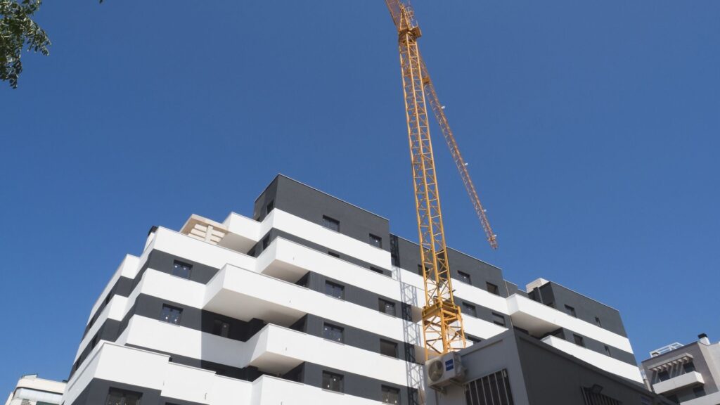 Modern apartment building under construction in Estepona, Costa del Sol, with crane against clear blue sky.