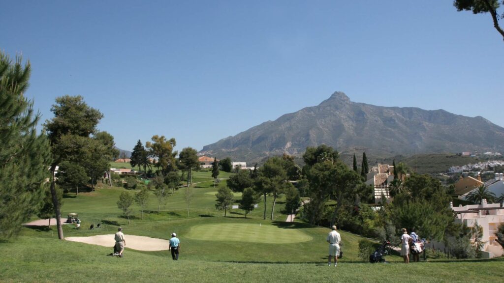 Golfers playing on a lush golf course in Marbella with panoramic views of La Concha mountain, highlighting golf properties in Marbella on the Costa del Sol under a clear blue sky.