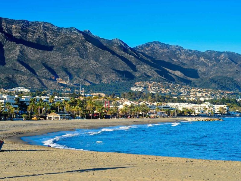 Beautiful beach and coastal skyline in Nueva Andalucía with mountains in the background, showcasing the area for new property developments in Marbella and highlighting the average rental yields for properties in Estepona.