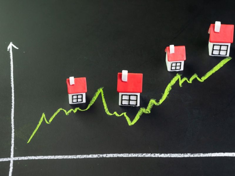 Rising property prices in Nueva Andalucía shown with miniature houses on an upward graph, illustrating growth in the real estate market and highlighting the average property prices in Nueva Andalucia.