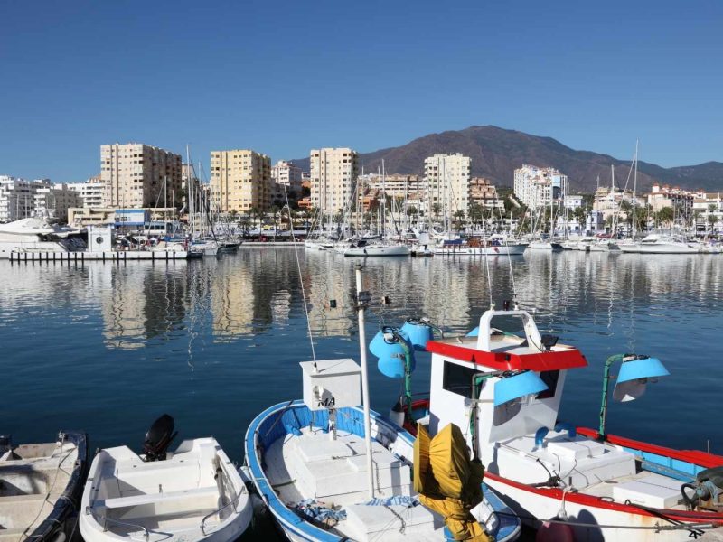 Estepona marina with fishing boats, yachts, and waterfront apartments under a clear blue sky on the Costa del Sol